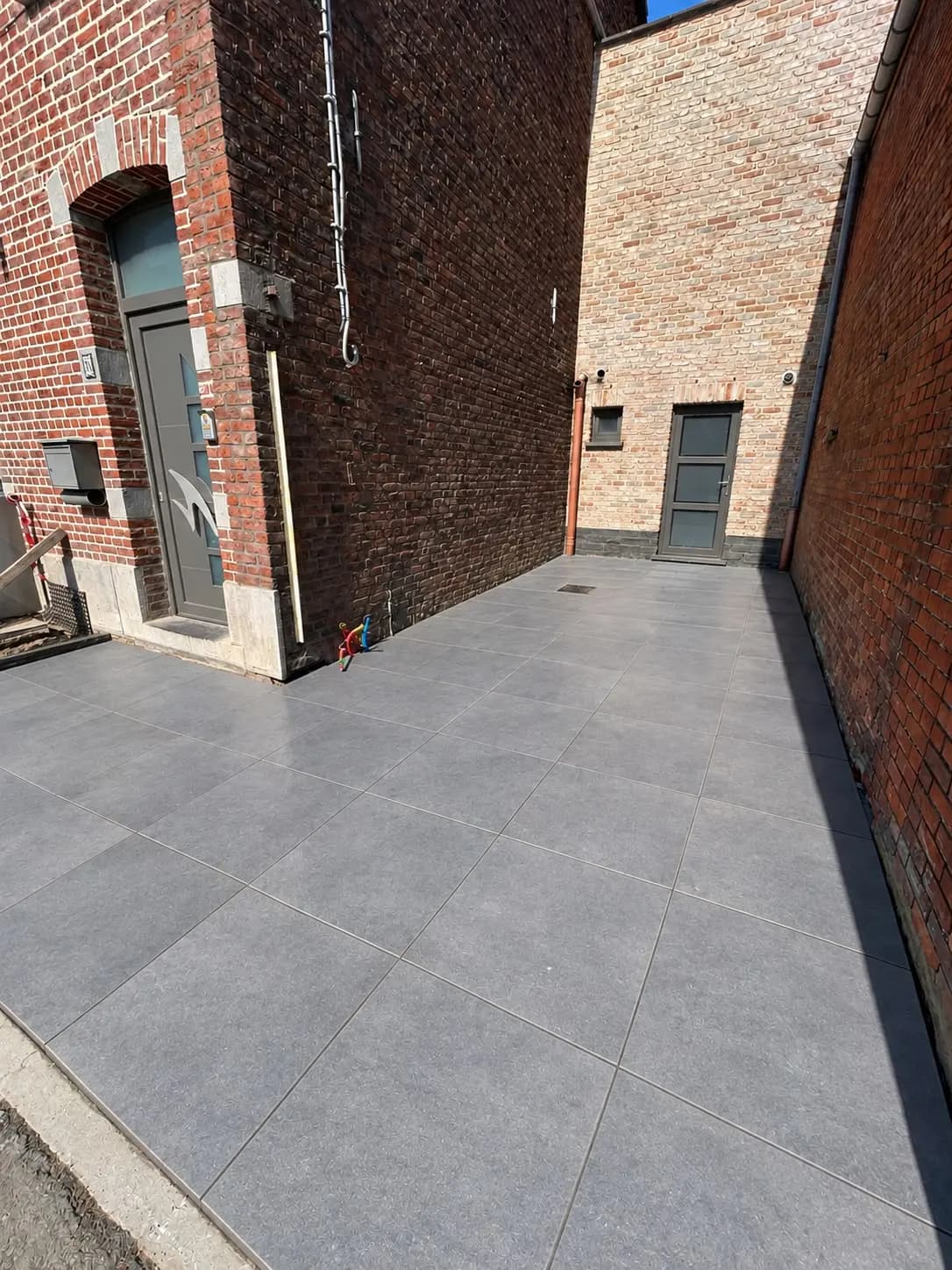 Cour entre deux façades en briques, entièrement carrelée en grand format gris par Km pose