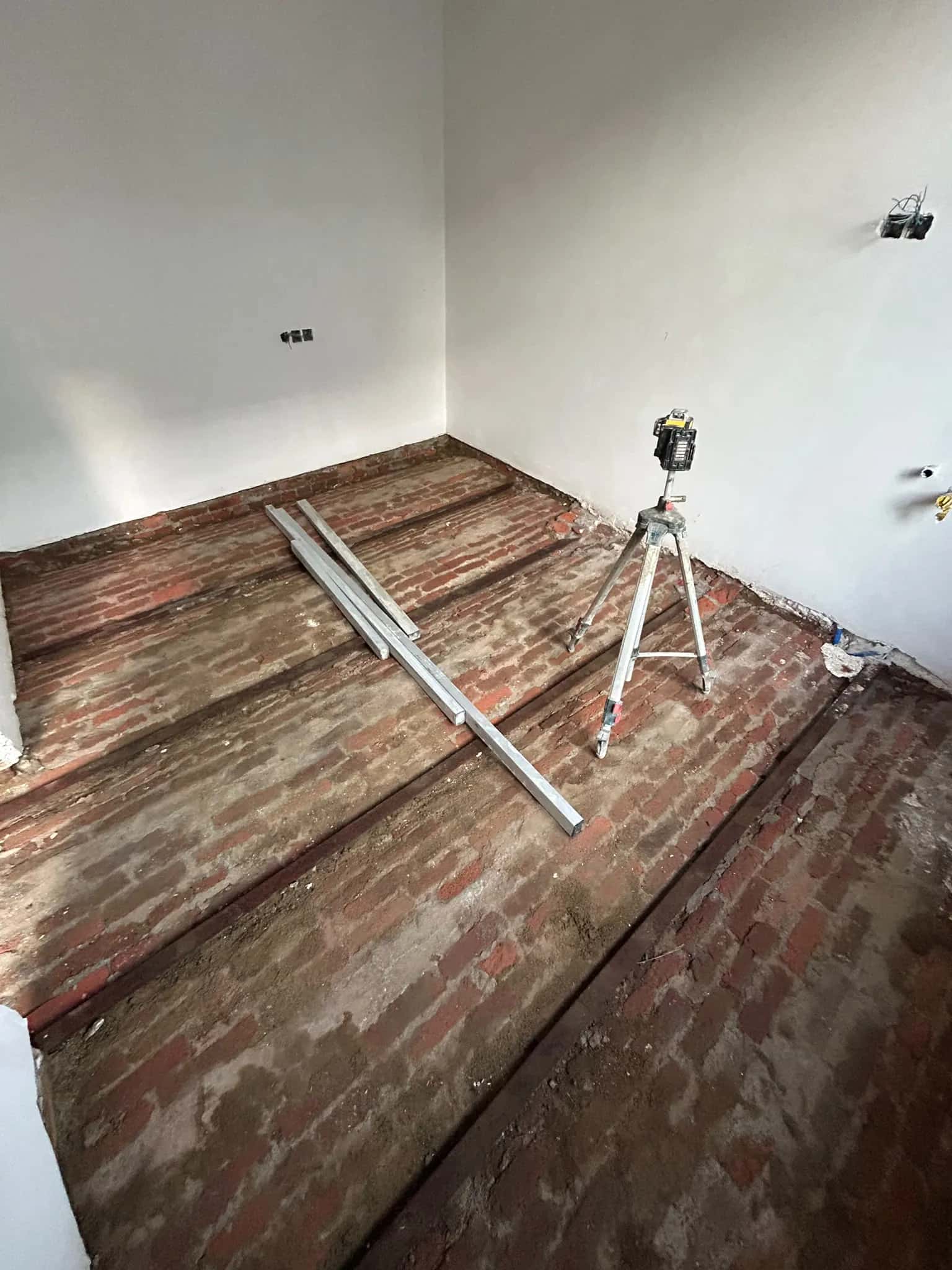 Niveau laser sur trépied et règles de guidage posées sur l'ancien sol en briques