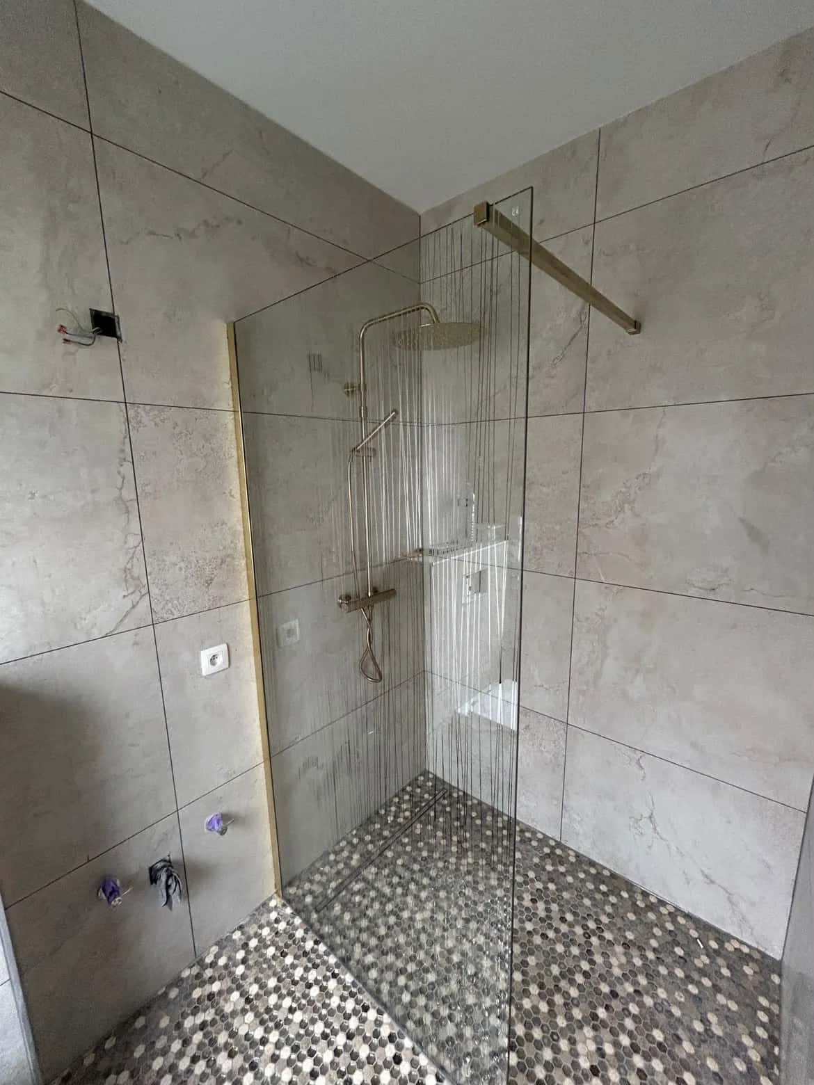 Douche à l'italienne terminée, paroi vitrée et robinetterie dorée sur le sol en mosaïque