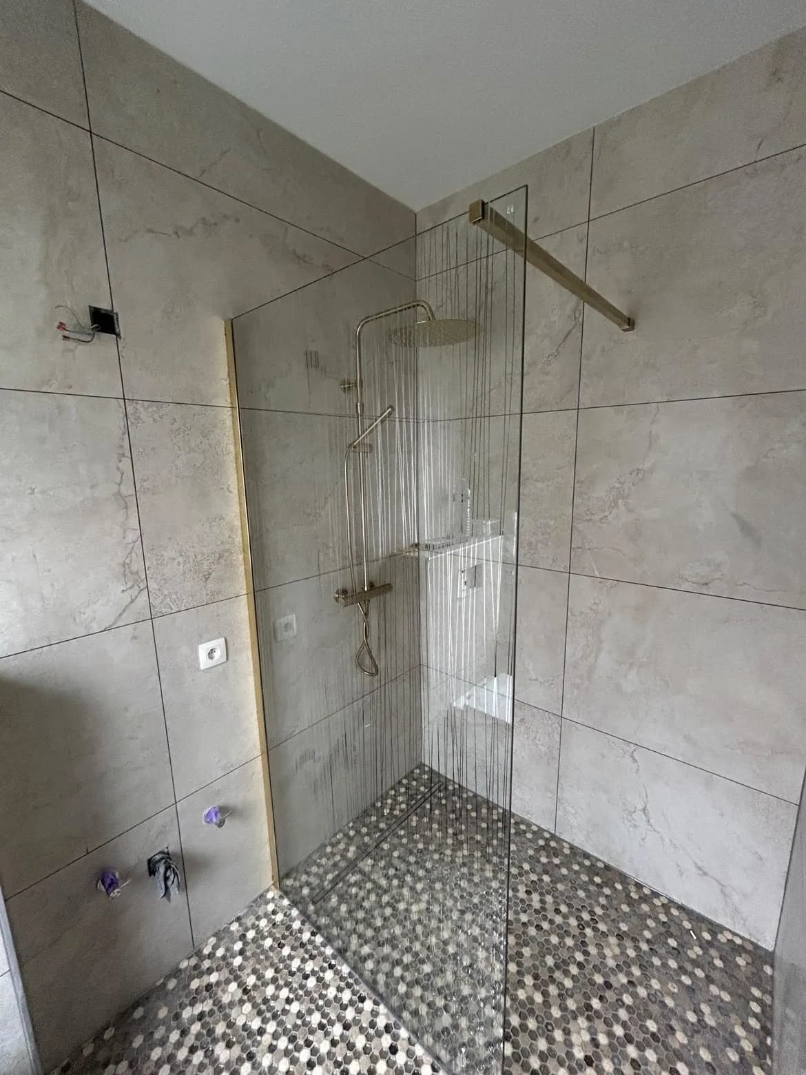 Douche à l'italienne terminée, paroi vitrée et robinetterie dorée sur le sol en mosaïque