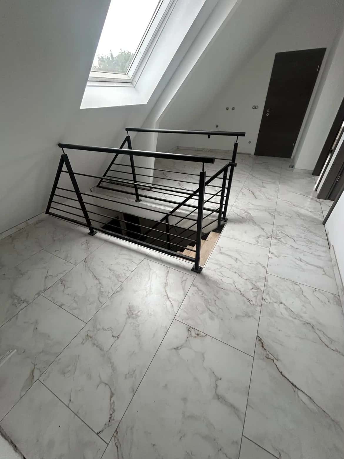 Palier sous combles carrelé en grand format effet marbre blanc, autour de la trémie d'escalier