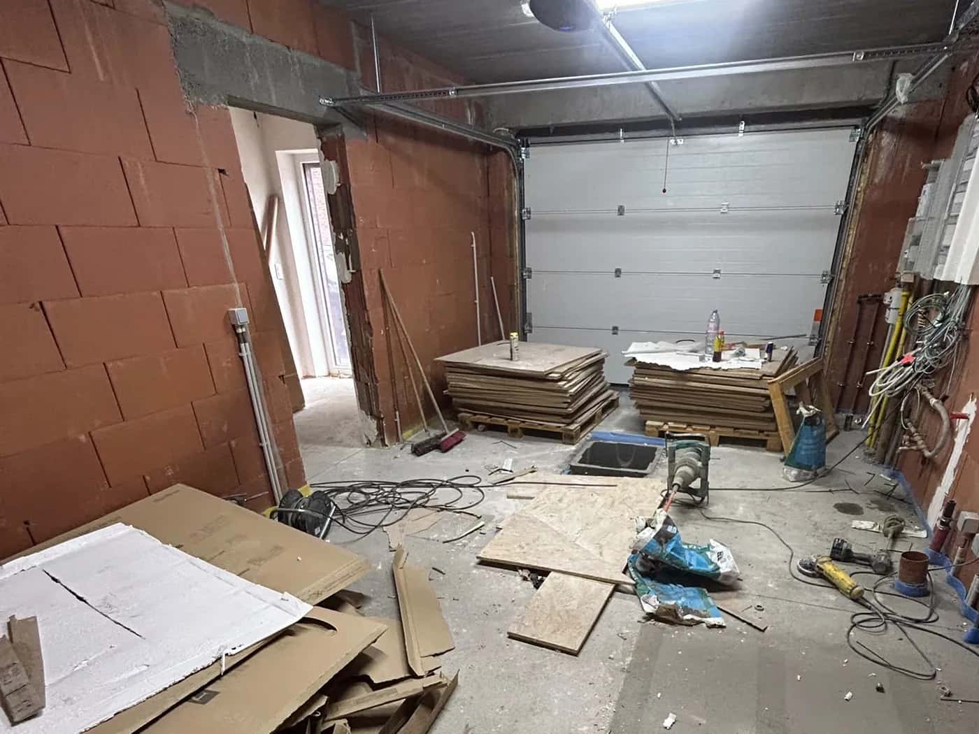 Garage avant la pose : dalle béton brute, palettes de carreaux et emballages au sol