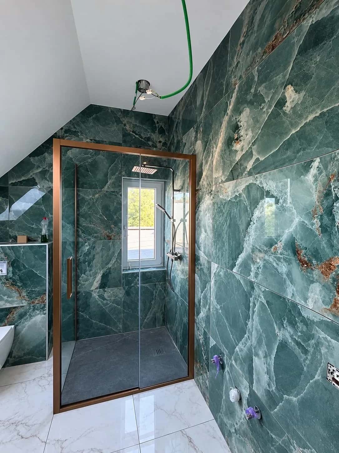 Douche à l'italienne fermée par une paroi cuivrée, murs en marbre vert sous la pente de toit