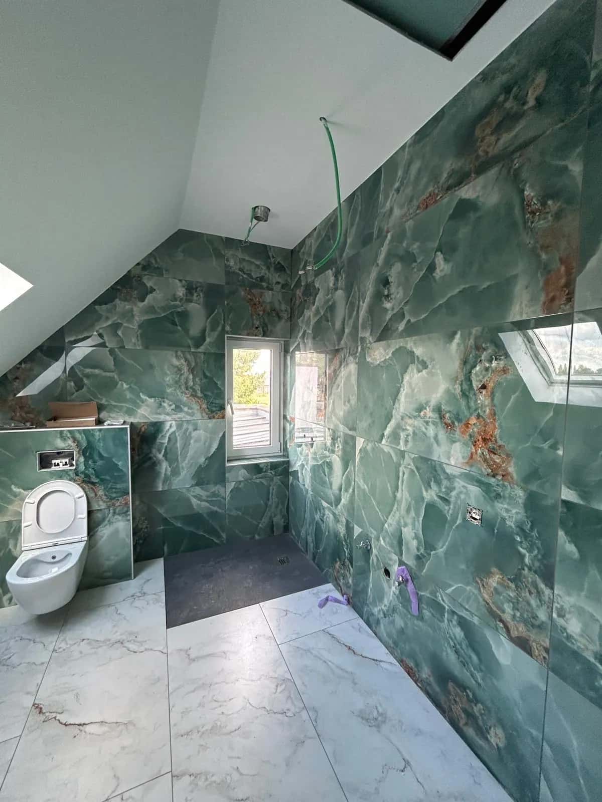 Salle de bain en grand format effet marbre vert, toilette suspendue et douche à l'italienne
