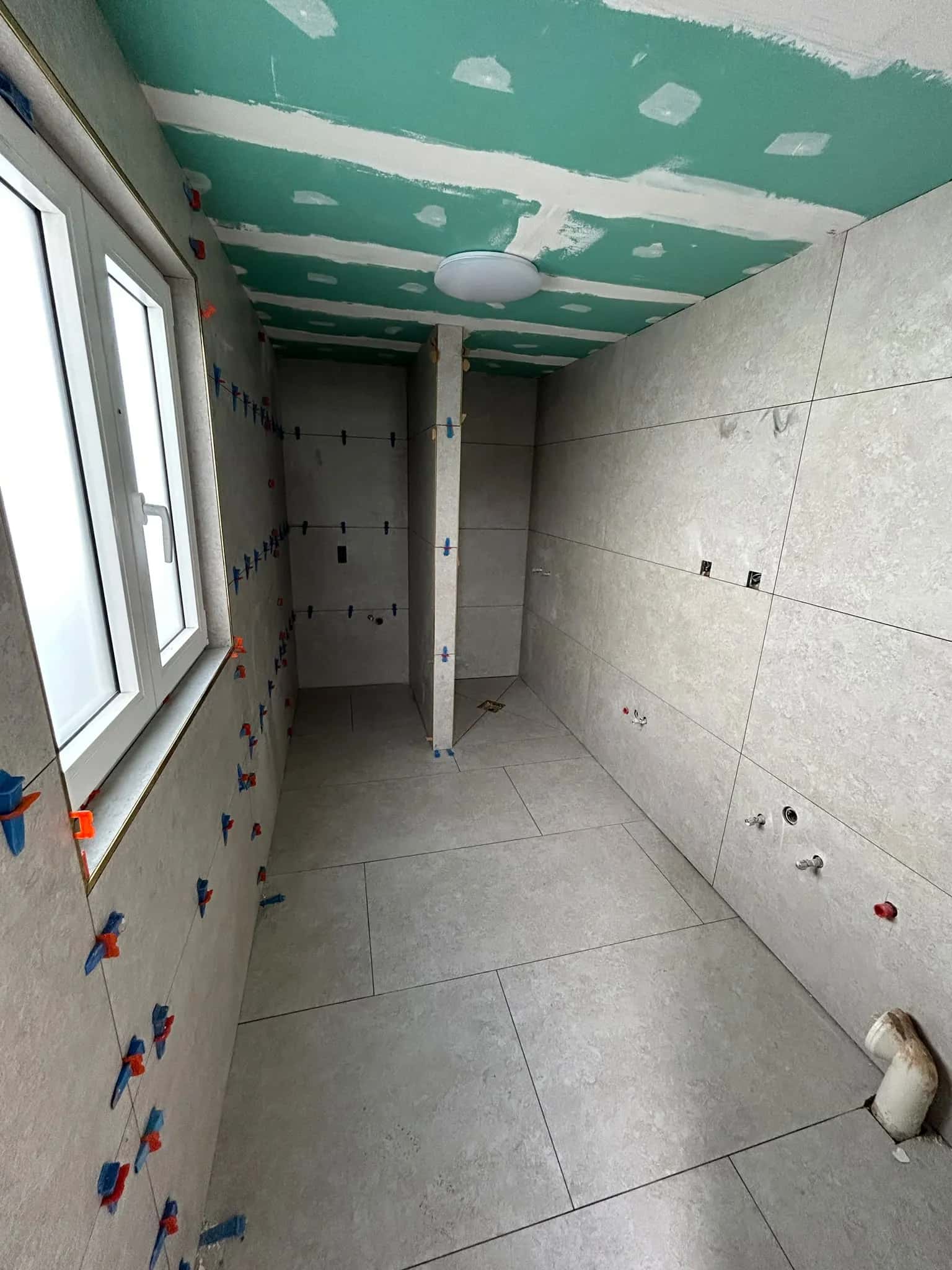 Salle de bain : murs carrelés en grand format, niveleurs encore en place