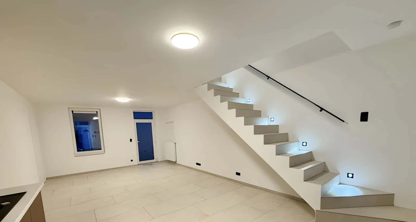 Séjour au sol carrelé et escalier aux marches carrelées, éclairé par des spots encastrés