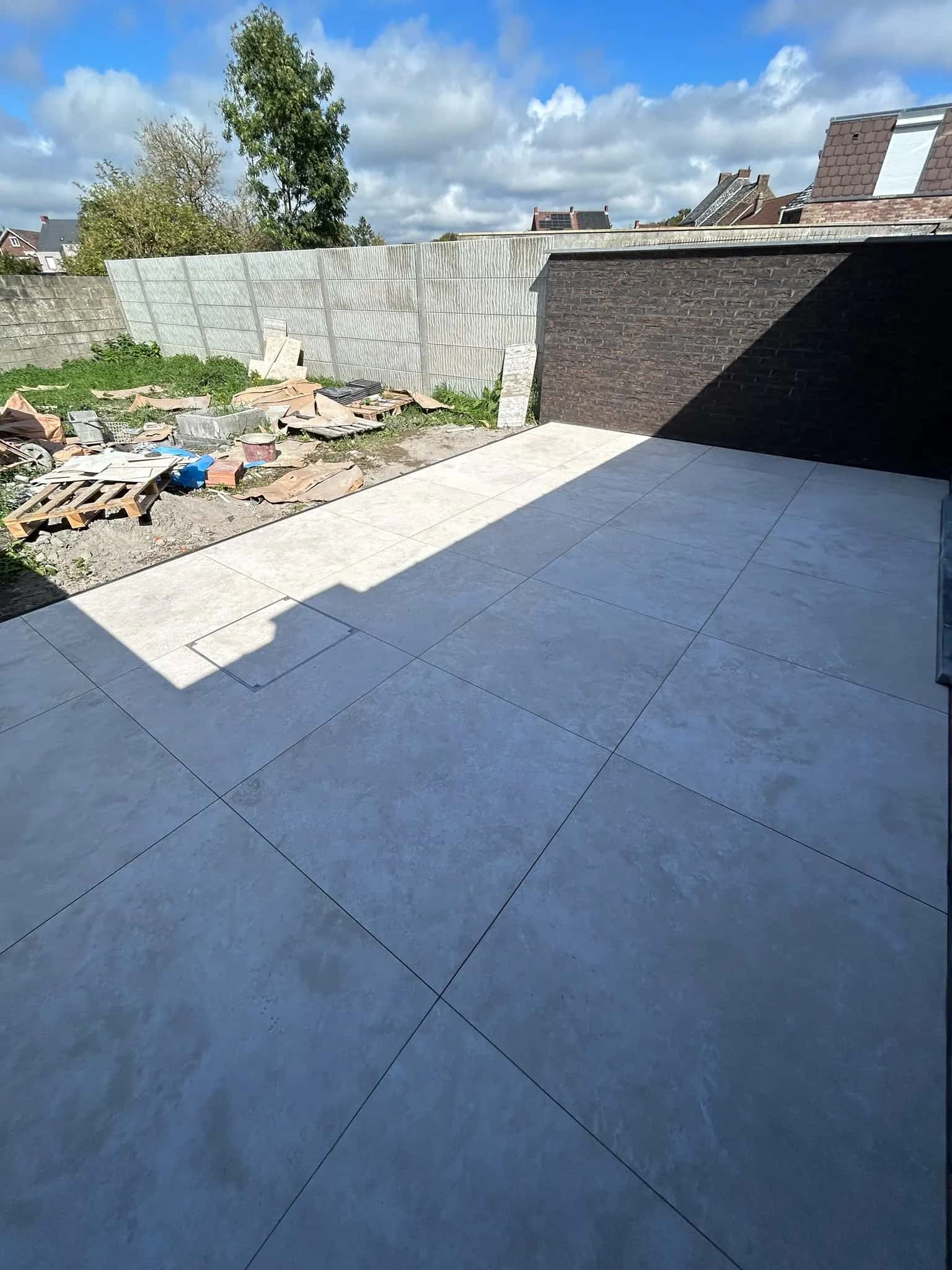 Terrasse carrelée le long du mur en briques, jardin encore à aménager