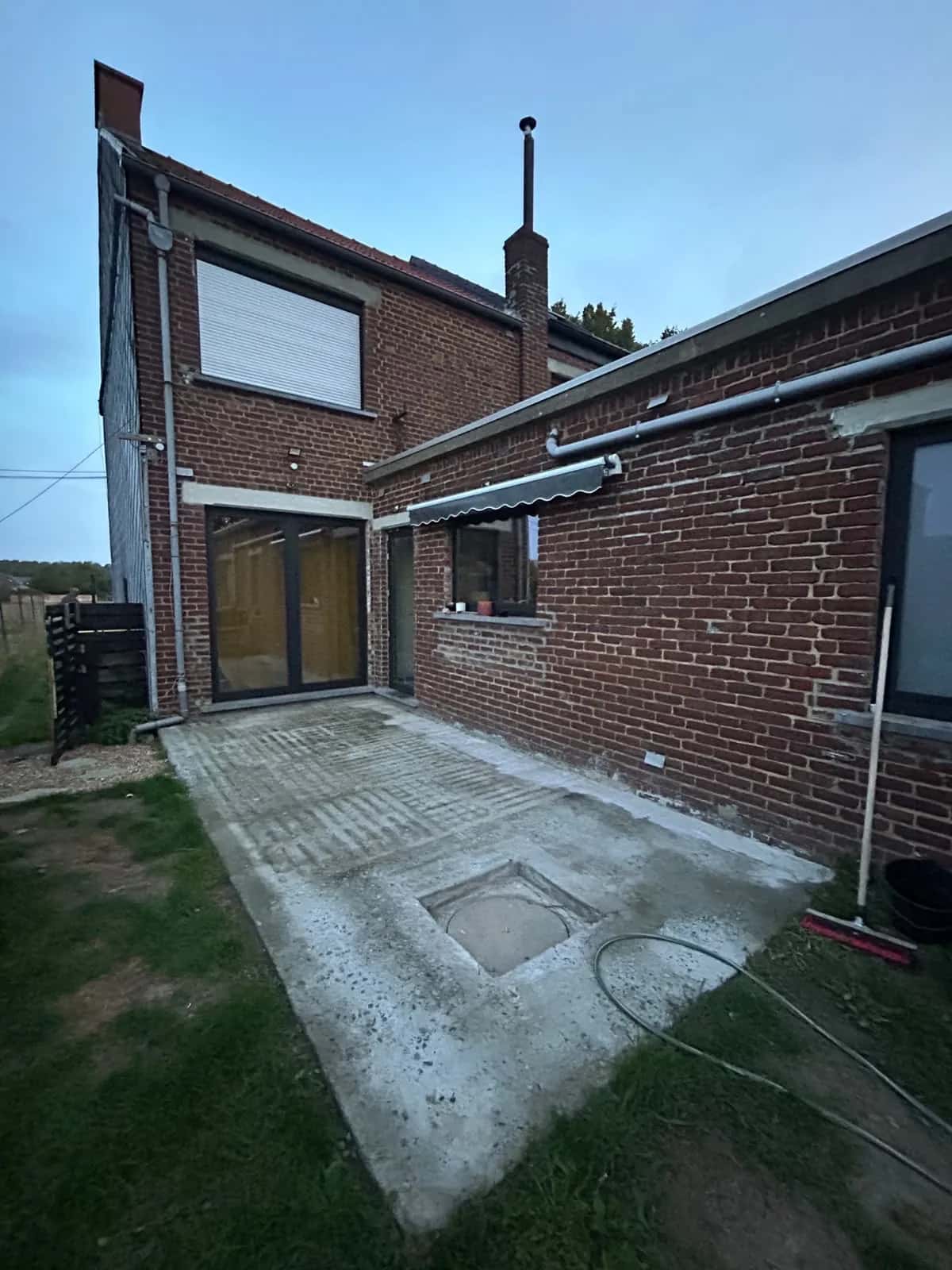 La cour avant le chantier : dalle béton brute et regard d'évacuation apparent