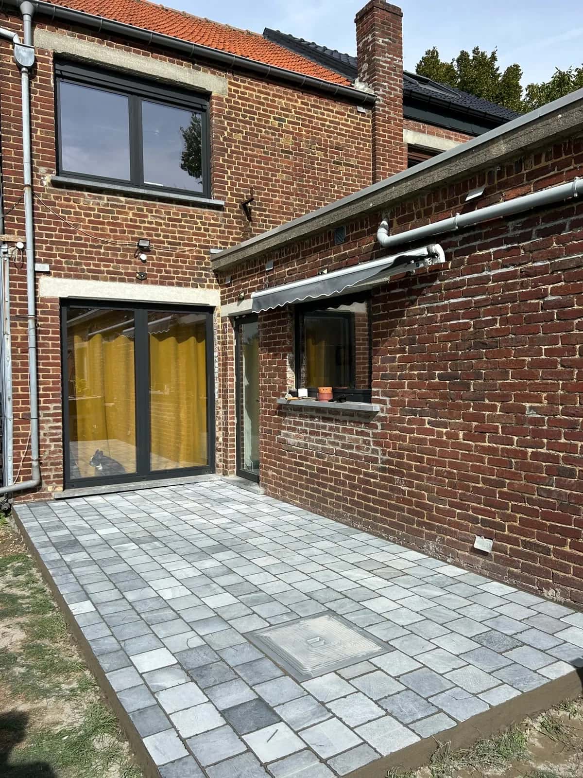 Cour arrière entièrement pavée, vue depuis le fond du jardin