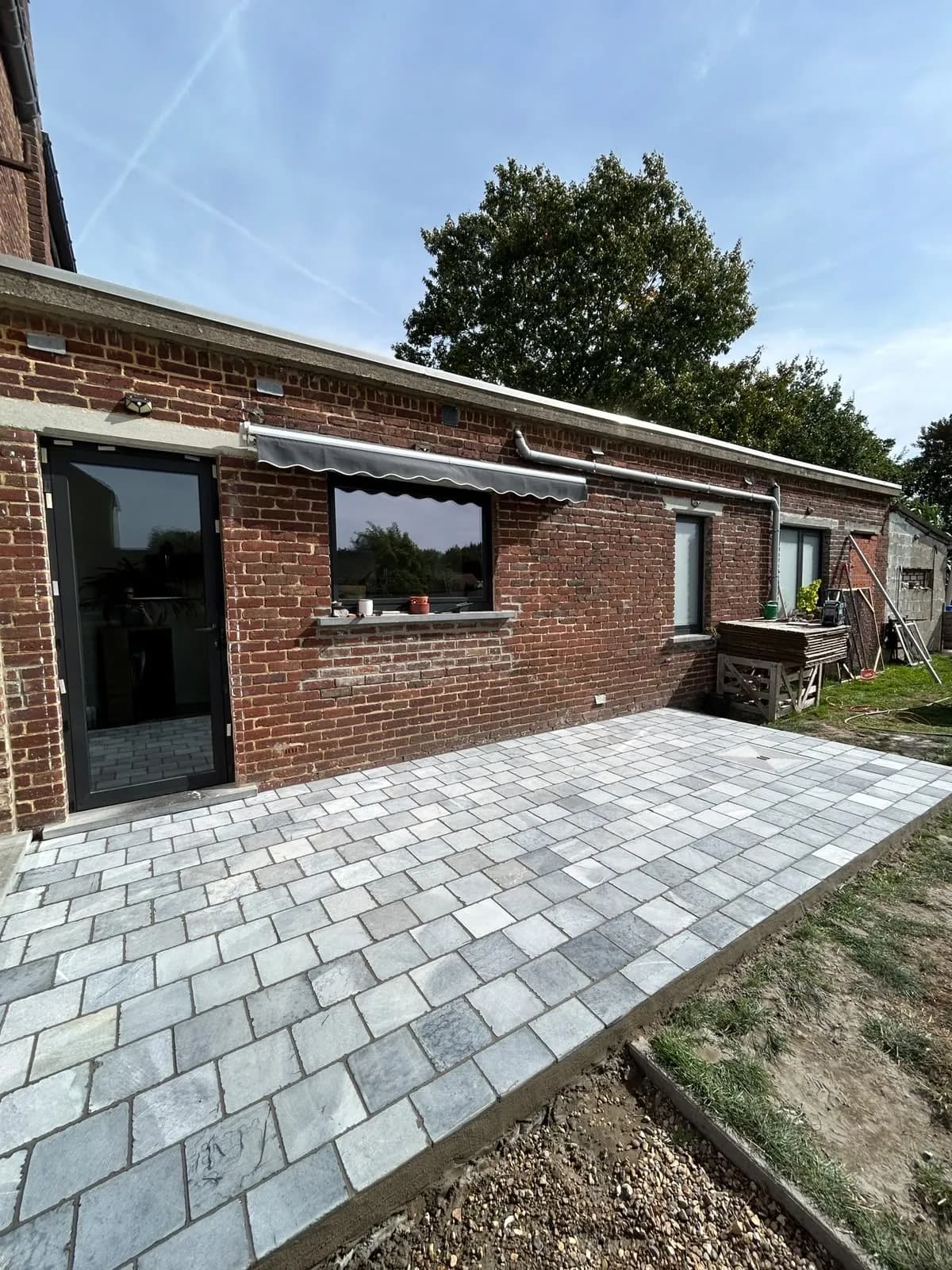 Terrasse en pavés effet pierre posée par Km pose le long de l'aile de la maison