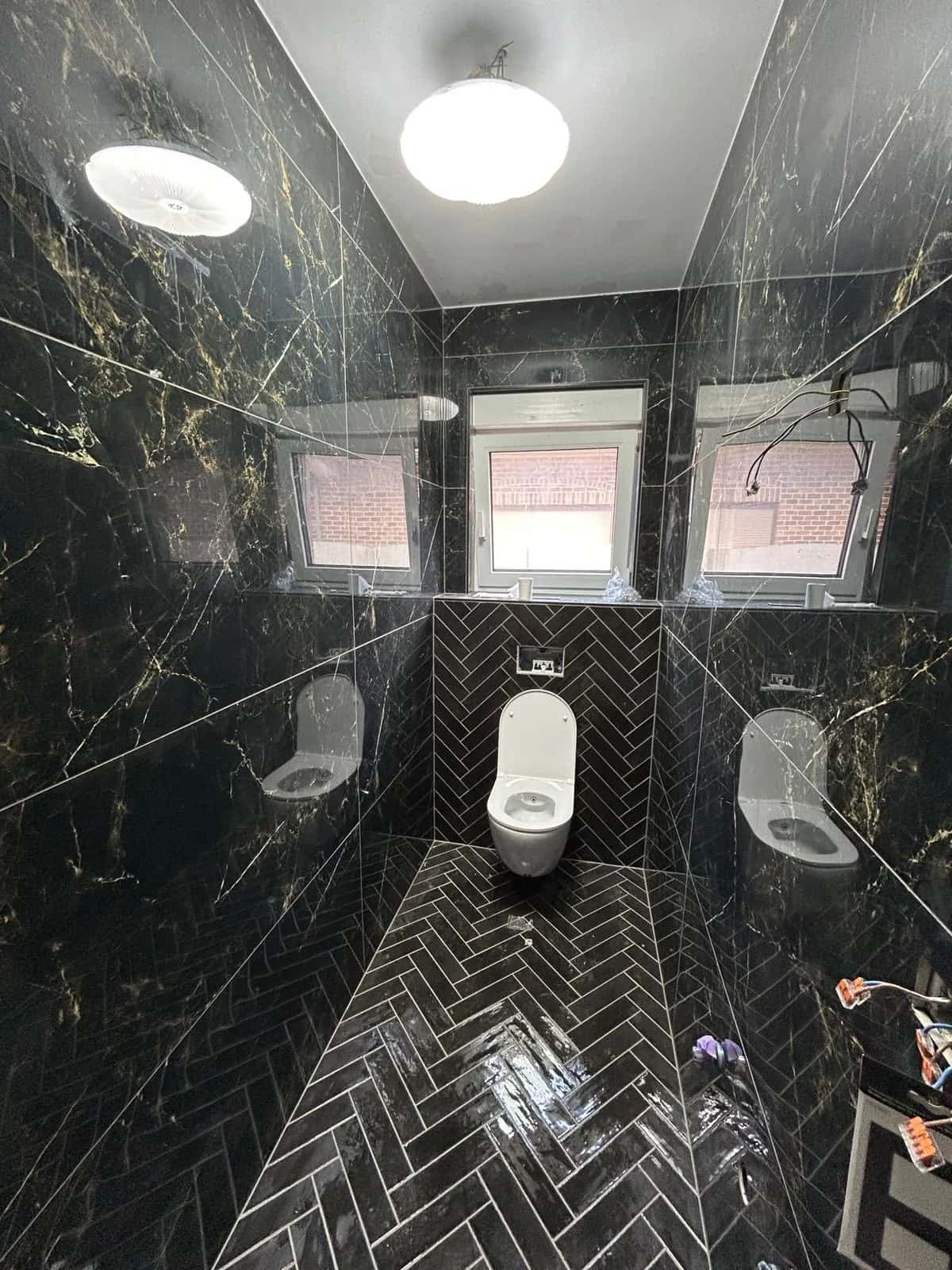 Toilettes habillées de faïence effet marbre noir, chevron au sol et sur le mur du fond