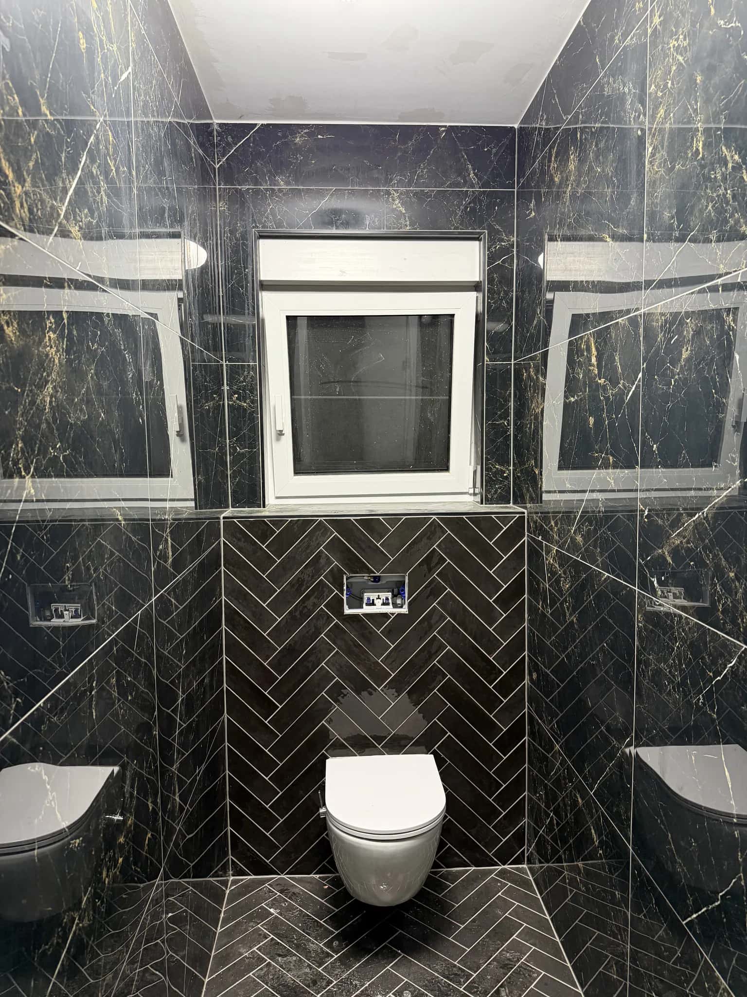 Mur du fond des toilettes en carreaux posés en chevron, encadré par le marbre noir
